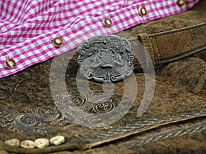 Close up bavarian lether belt with coat of arms on lederhose and pink check shirt, traditional clothing for Oktoberfest photo