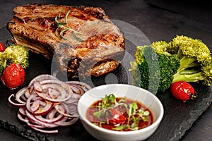 Close-up BBQ pork loin with spicy sauce and vegetables on a black stone board. Selective focus. Old rustic wooden background