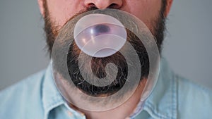 Close-up of a bearded man`s mouth chewing chewing gum. Man blowing out a bubble of bubble gum
