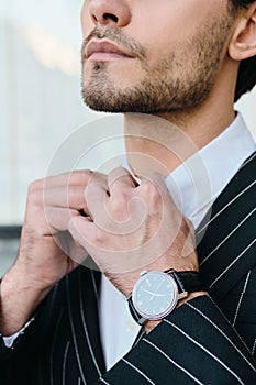 Close up bearded man in white shirt and classic striped jacket with wristwatch on city street alone