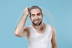 Close up bearded young man 20s years old examining his hair in white shirt isolated on blue pastel wall background