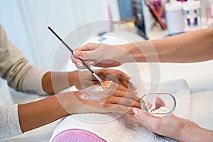 Close-up of beautician applying cream on woman`s hand using brus