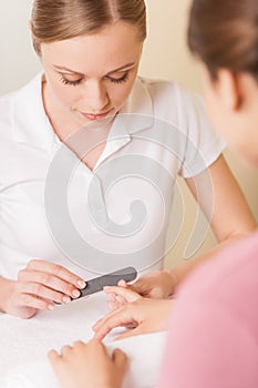 Close-up of beautician hand filing nails of woman in salon.