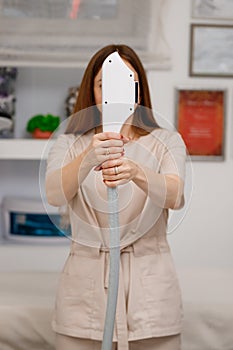 Close up of beautician hand in glove holding ultrasound device for face and skin lifting procedure and hair removal. Young woman