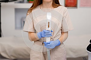 Close up of beautician hand in glove holding ultrasound device for face and skin lifting procedure and hair removal. Young woman