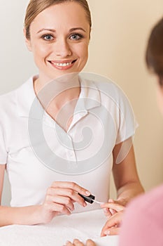 Close-up of beautician hand painting nails of woman in salon.