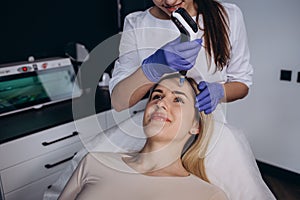 Close up of beautician hands in sterile gloves using dermapen during skincare procedure. Young woman receiving facial photo