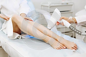 Close up of beautician removing hair on lady leg with laser epilation machine