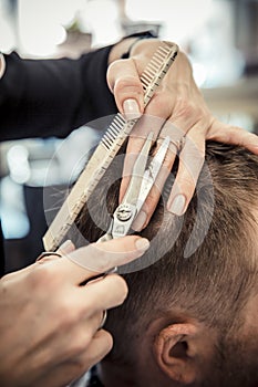 Close up of beautician's hand giving a haircut to male customer at parlor.