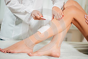 Close-up Of A Beautician Waxing Woman Leg With Wax Strip At Beauty Spa