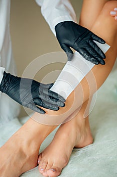 Close-up Of A Beautician Waxing Woman Leg With Wax Strip At Beauty Spa