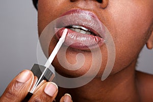 Close up beautiful african american woman applying shiny lip gloss