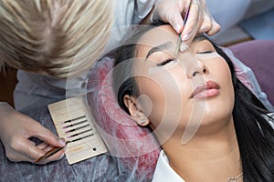 Close-up of a beautiful asian woman on eyelash extension procedure. Double volume false eyelashes. Lashmaker at work.