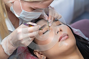 Close-up of a beautiful asian woman on eyelash extension procedure. Double volume false eyelashes. Lashmaker at work.