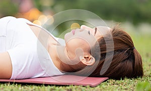 Close up Beautiful Attractive Asian woman practice yoga Dead Body pose or Savasana pose lying on green grass for yoga Meditation f