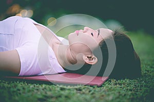 Close up Beautiful Attractive Asian woman practice yoga Dead Body pose or Savasana pose lying on yoga mat with green grass for yog