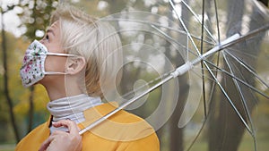 Close up. Beautiful blond woman with face mask holding transparent umbrela in the park in autumn