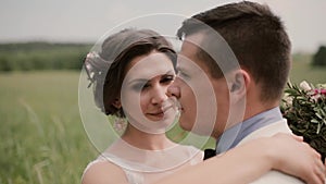 Close-up of a beautiful bride. She hugs her groom and tenderly looks in camera then into his eyes. Wedding day