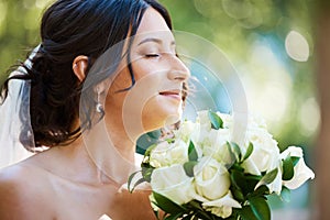 Close up of a beautiful bride smelling her wedding bouquet.Tender bride standing outside on a sunny day and smelling