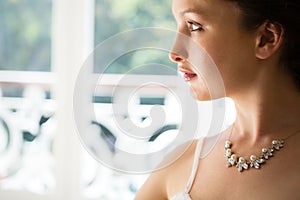 Beautiful bride wearing necklace looking through window at home