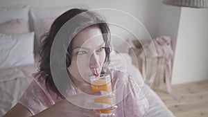 Close-up of beautiful brunette caucasian woman drinking orange juice and smiling. Portrait of attractive young lady