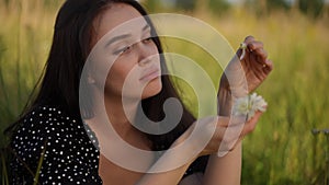 Close-up. A beautiful brunette girl rips off petals from a white wildflower in her hand and blows them off her palm