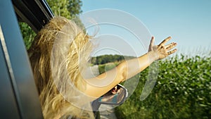 CLOSE UP: Beautiful Caucasian girl waves her arm while driving down rural road