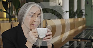 Close up of beautiful elderly businesswoman sitting at table and enjoing drinking coffee. Old lady boss having break in