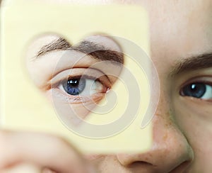 Close-up of the beautiful eyes of a young girl looking through a wooden heart stencil. Symbol of love and all lovers. Concept of l