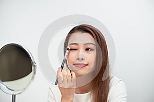 Close up of beautiful face of asian young woman getting make-up. Asian woman is applying eyeshadow on her eyebrow with brush.