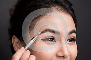 Close up of beautiful face of young asian woman getting make-up. The artist is applying eyeshadow on her eyebrow with brush