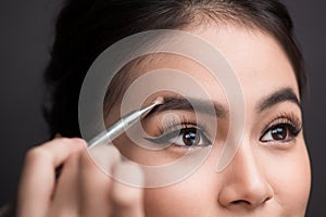 Close up of beautiful face of young asian woman getting make-up. The artist is applying eyeshadow on her eyebrow with brush