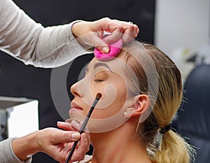 Close up of beautiful face of young woman getting make-up, using a brush, the lady closed eyes with relaxation, in a