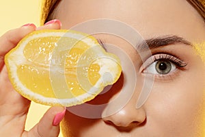 Close up of beautiful female face with lemon slice over yellow background. Cosmetics and makeup, natural and eco