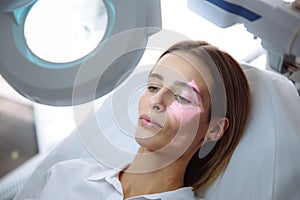 Close-up beautiful female face with vein scanner and cosmetologist`s hands with syringe during facial beauty injections