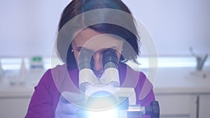 Close-up. A beautiful female gynecologist in a purple medical suit directs a binocular video colposcope into the camera