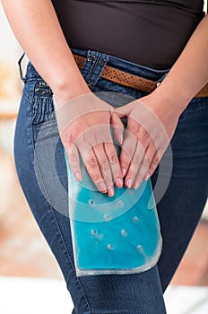 Close up of a beautiful female holding ice gel pack on leg, medical concept, in office background