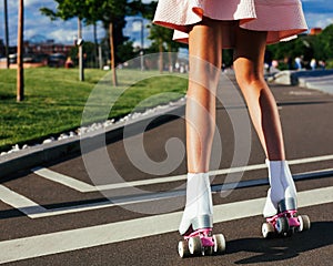 Close-up of beautiful female legs on roller skates in a steep summer outfit on the road