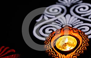 Close up beautiful glowing clay lamp and red white and rangoli art on black background with copy space. diwali concept