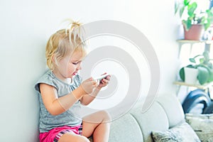 Close up Beautiful little baby girl holding and playing with smart phone on the white wall background. Children and technology con