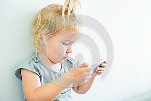 Close up Beautiful little baby girl holding and playing with smart phone on the white wall background. Children and technology con