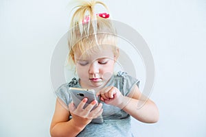 Close up Beautiful little baby girl holding and playing with smart phone on the white wall background. Children and technology con