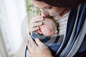 Close up, beautiful mother kissing her son in sling