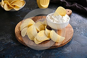 Close-up of beautiful potato chips and sauce in a white bowl on a wooden cutting board.