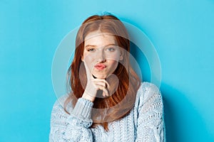 Close-up of beautiful redhead girl thinking, pucker lips and staring thoughtfula t camera, making choice, standing over