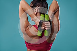 Close-up of a beautiful strong muscular back of a toned woman holding dumbbells and pumping triceps muscles. Healthy lifestyle