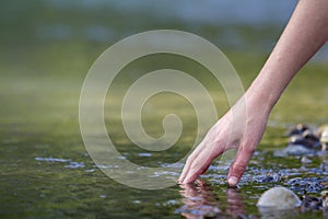 Close-up of beautiful white woman hand tenderly touching, scooping clean fresh sweet water on blurred green copy-space background