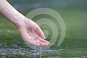 Close-up of beautiful white woman hand tenderly touching, scooping clean fresh sweet water on blurred green copy-space background