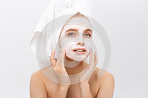 Close-up beautiful woman applying moisturizer cosmetic cream on face on light background.