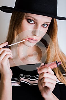 Closeup of beautiful woman applying pink lipstick on lips againstwhite background